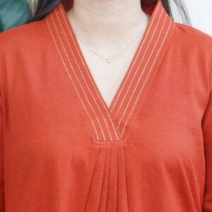 Model wearing a solid rust-colored A-line kurta with V-neck embroidery and side pockets, paired with black pants.