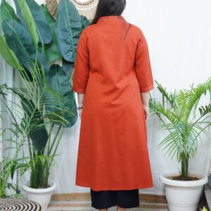 Model wearing a solid rust-colored A-line kurta with V-neck embroidery and side pockets, paired with black pants.